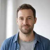 Portrait d’Aymeric Lebreton, cheveux châtains courts, chemise en jean, fond de pièce lumineuse et floue