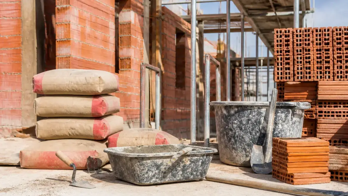 Sac de ciment, briques, seau sur chantier de maçonnerie avec comptoir-du-btp.fr en arrière-plan