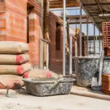 Sac de ciment, briques, seau sur chantier de maçonnerie avec comptoir-du-btp.fr en arrière-plan