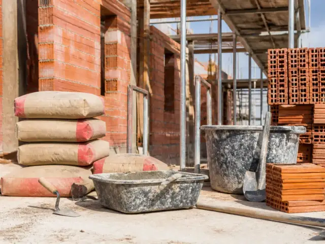 Sac de ciment, briques, seau sur chantier de maçonnerie avec comptoir-du-btp.fr en arrière-plan