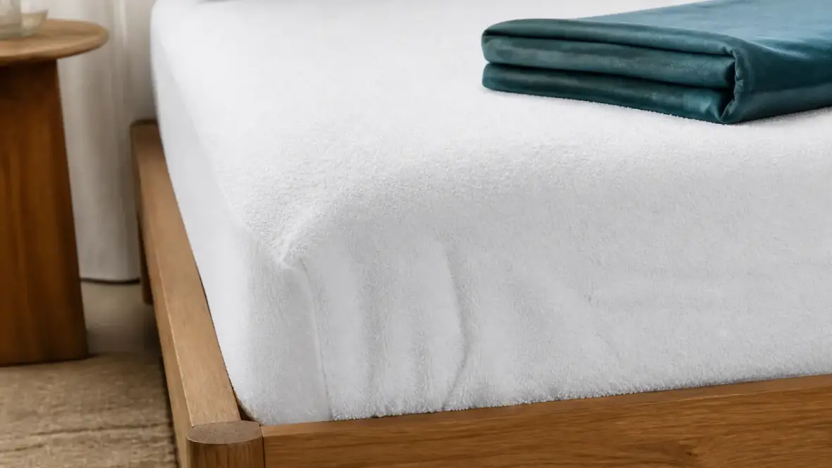 Coin de matelas recouvert d’une alèse blanche à bonnets élastiqués, drap-housse replié à côté