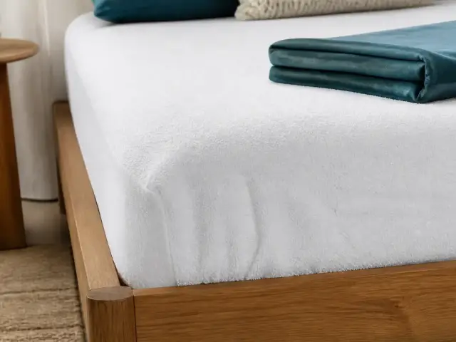 Coin de matelas recouvert d’une alèse blanche à bonnets élastiqués, drap-housse replié à côté