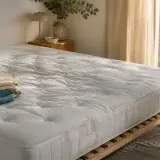Matelas blanc posé sur un sommier à lattes, vu de biais, avec un léger creux visible au milieu de la surface