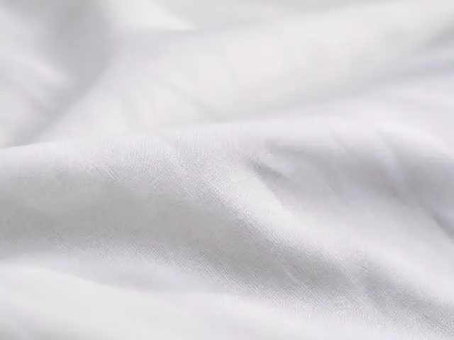 Gros plan sur un drap blanc en percale de coton, tissage fin et serré, surface mate légèrement froissée