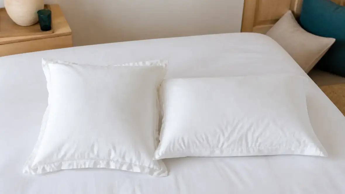 Un oreiller carré et un oreiller rectangulaire posés l’un à côté de l’autre sur un lit, dans des taies blanches