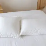 Un oreiller carré et un oreiller rectangulaire posés l’un à côté de l’autre sur un lit, dans des taies blanches