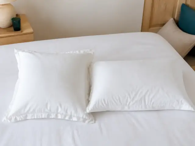 Un oreiller carré et un oreiller rectangulaire posés l’un à côté de l’autre sur un lit, dans des taies blanches