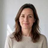 Portrait d’Ombeline Garrigues, cheveux bruns mi-longs, pull côtelé couleur lin, fond de pièce claire et floue