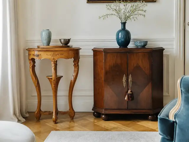 Deux meubles côte à côte, une petite table aux pieds sculptés en tiges végétales et un cabinet géométrique en bois sombre